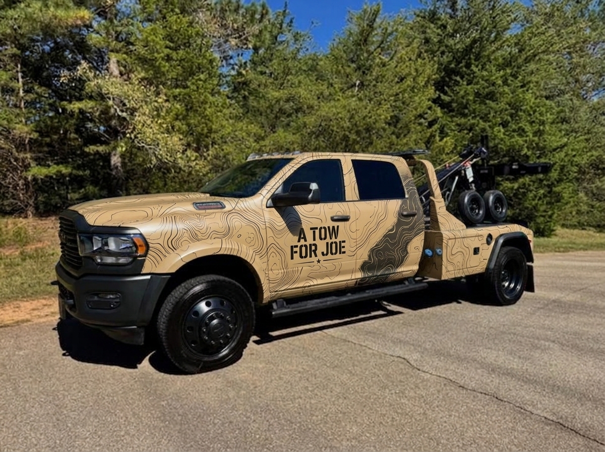 A Tow for Joe branded tow truck with topographic map wrap parked on a road